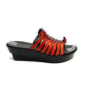 May include: Orange leather woven sandals with a black platform wedge heel. The sandals have a strap across the toe and an ankle strap with a small buckle. The brand name "DONALD J PLINER" is printed on the insole.