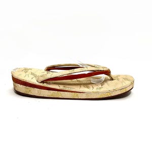 May include: A pair of cream-colored sandals with a red strap and a gold floral pattern. The sandals have a platform sole.