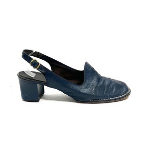 Könnte beinhalten: Ein Paar dunkelblaue Lederschuhe mit Absatz und Slingback-Riemen mit einer goldenen Schnalle.