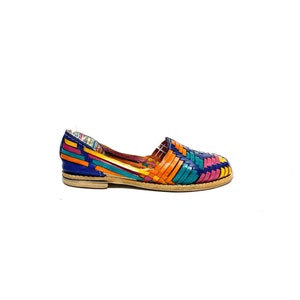 May include: A brightly coloured woven leather flat shoe. The shoe has a vibrant pattern of blue, orange, teal, and pink woven leather straps. The sole is light brown. The shoe is a slip-on style.