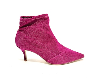 May include: A fuchsia-colored ankle boot with a pointed toe and a small, thin heel. The boot has a textured, glittery appearance and a stretchy, sock-like upper. The heel is approximately 2 inches tall.