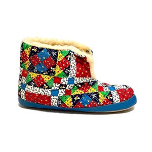 May include: A colorful patchwork bootie with a blue sole and cream-colored faux fur trim. The bootie features a quilted design with red, blue, yellow, and green fabric squares. The bootie is designed for indoor wear.