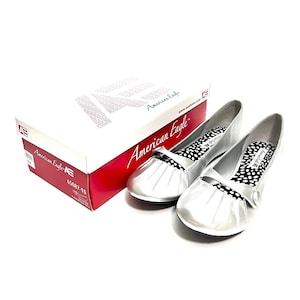 May include: A pair of silver ballet flats with pleated vamps and black and white polka dot insoles. The shoes are next to a white and red box with the text "American Eagle". The box has the number "65087-15".
