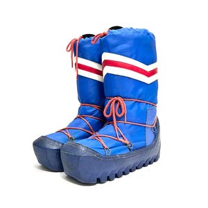 May include: A pair of blue snow boots with red and white accents. The boots have a high-top design with red laces and a thick, ridged sole. The boots are made of a nylon-like material.