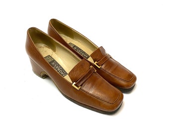 May include: A pair of brown leather heeled loafers with a gold buckle. The shoes have a square toe and are made by Givenchy.