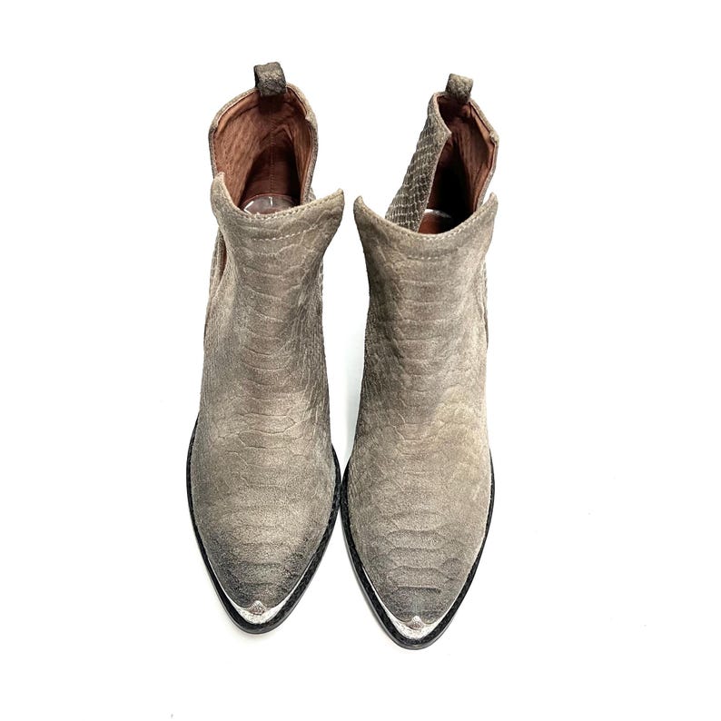 May include: A pair of grey suede ankle boots with a pointed toe and silver metal accents. The boots have a textured, snake-like pattern and a stacked heel. The interior is a warm brown colour.
