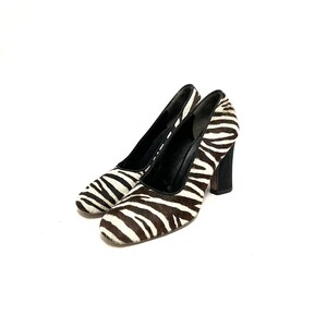 Pode incluir: Um par de sapatos de salto alto de zebra preto e branco com salto bloco.