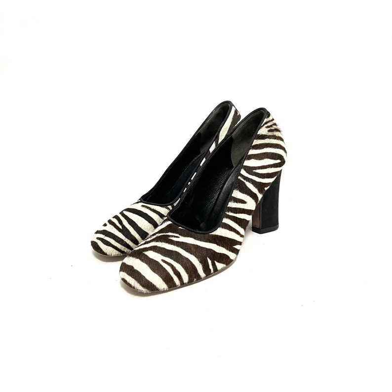 Pode incluir: Um par de sapatos de salto alto de zebra preto e branco com salto bloco.