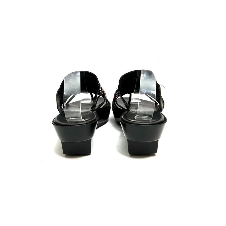 May include: A pair of black leather heeled sandals with a criss-cross strap design. The sandals have a slingback strap and a wedge heel.