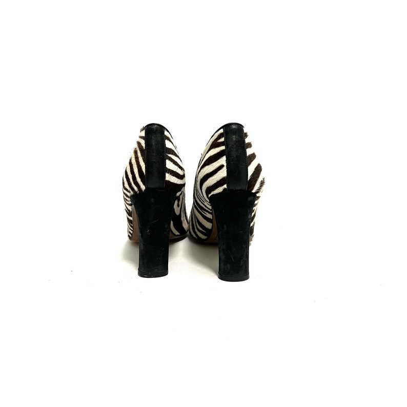 Pode incluir: Um par de sapatos de salto alto de zebra preto e branco com saltos pretos.