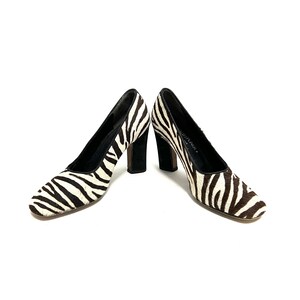 Pode incluir: Um par de sapatos de salto alto de zebra preto e branco com saltos pretos.