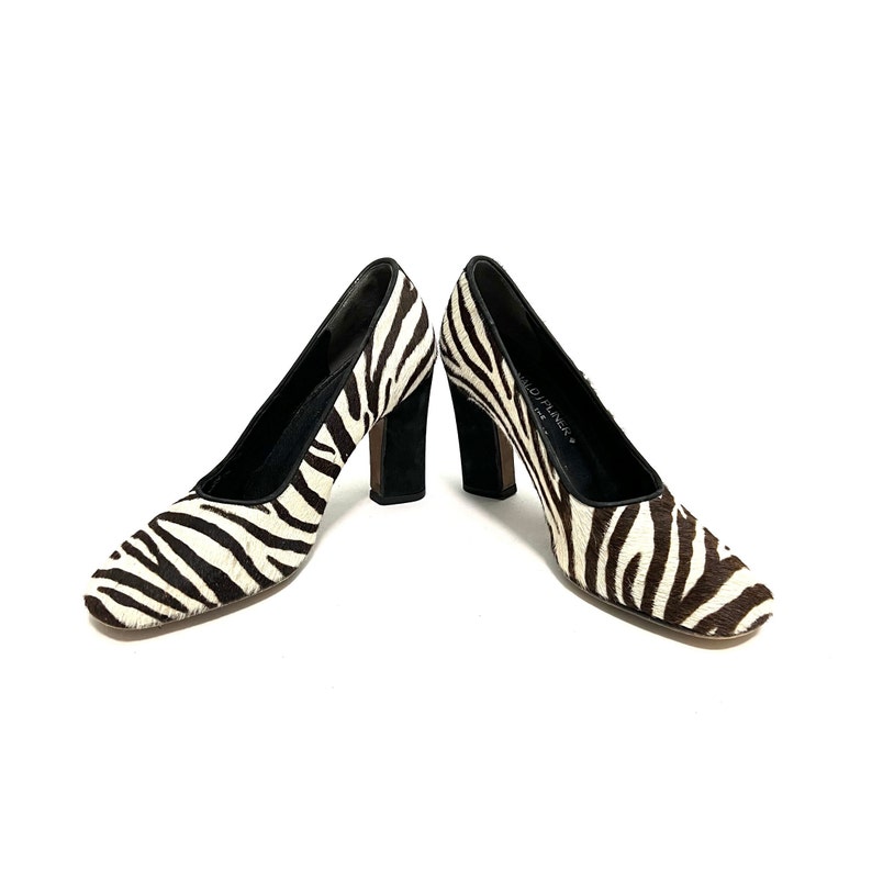 Pode incluir: Um par de sapatos de salto alto de zebra preto e branco com saltos pretos.