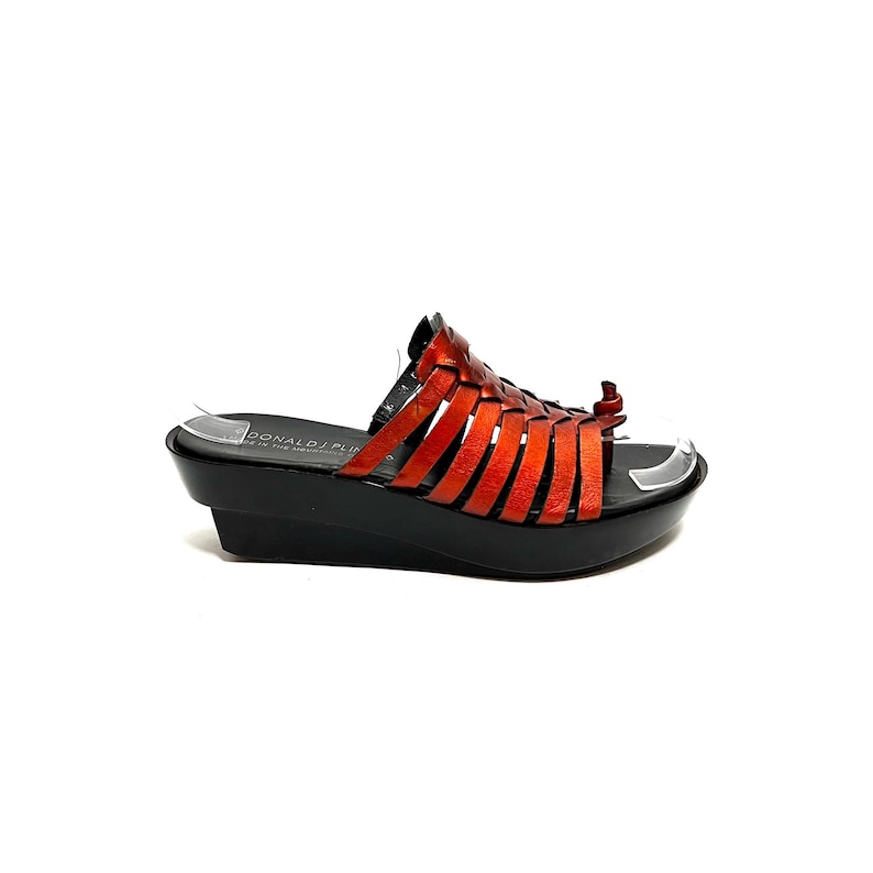 May include: Orange leather woven sandals with a black platform wedge heel. The sandals have a strap across the toe and an ankle strap with a small buckle. The brand name "DONALD J PLINER" is printed on the insole.