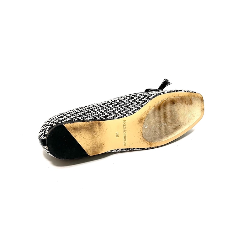 Op de afbeelding: Zwart-wit patroon ballerina's met een kleine strik en kwastjes. De schoen heeft een vierkante neus en een zwarte hak. De zool vertoont gebruikssporen. De merknaam "Enzo Angiolini" is zichtbaar op de zool.