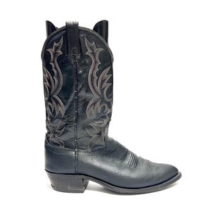 Op de afbeelding: Zwarte leren cowboylaars met decoratieve stiksels. De laars heeft een puntige neus, een gestapelde hak en een instapontwerp. De schacht is versierd met ingewikkelde geborduurde patronen in een contrasterende kleur.