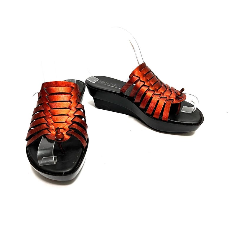 May include: A pair of orange leather sandals with woven straps and a wedge heel. The sandals have a black sole and are made by the brand "Somme."