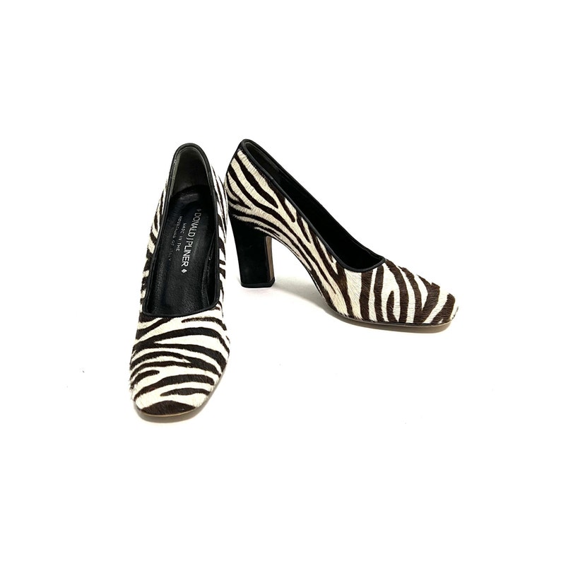 Pode incluir: Um par de sapatos de salto alto de zebra preto e branco com salto preto. Os sapatos s&atilde;o da marca Donald J Pliner.