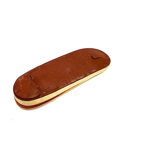 May include: A brown leather case with a flap closure. The case is lined with a cream-colored fabric.