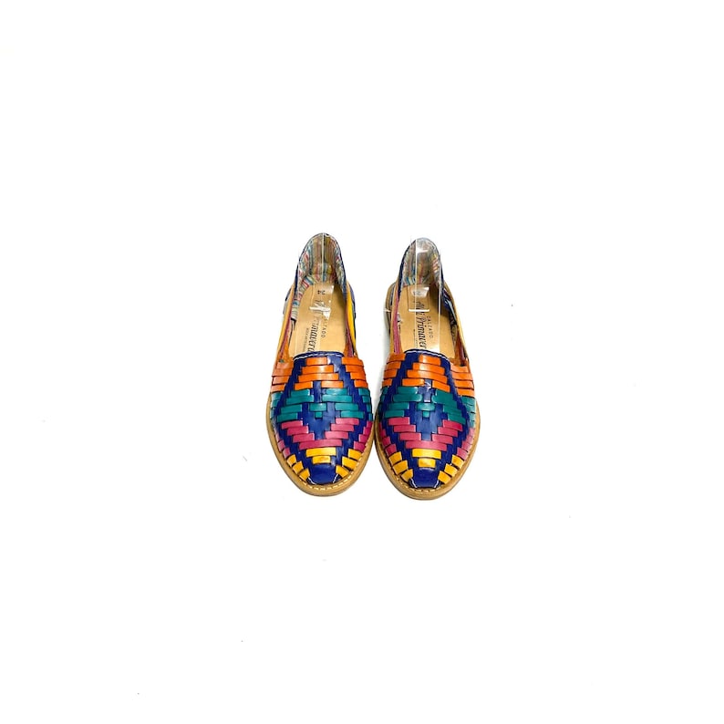May include: A pair of colourful woven leather flats. The shoes feature a vibrant pattern of orange, teal, pink, and blue leather strips. The soles are a light brown colour, and the interior has a patterned fabric lining. The shoes are displayed on a white background.