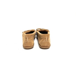 Puede incluir: Un par de mocasines de ante marr&oacute;n con un detalle de costura decorativa alrededor del borde del zapato. Los mocasines tienen una punta redondeada y una suela plana.