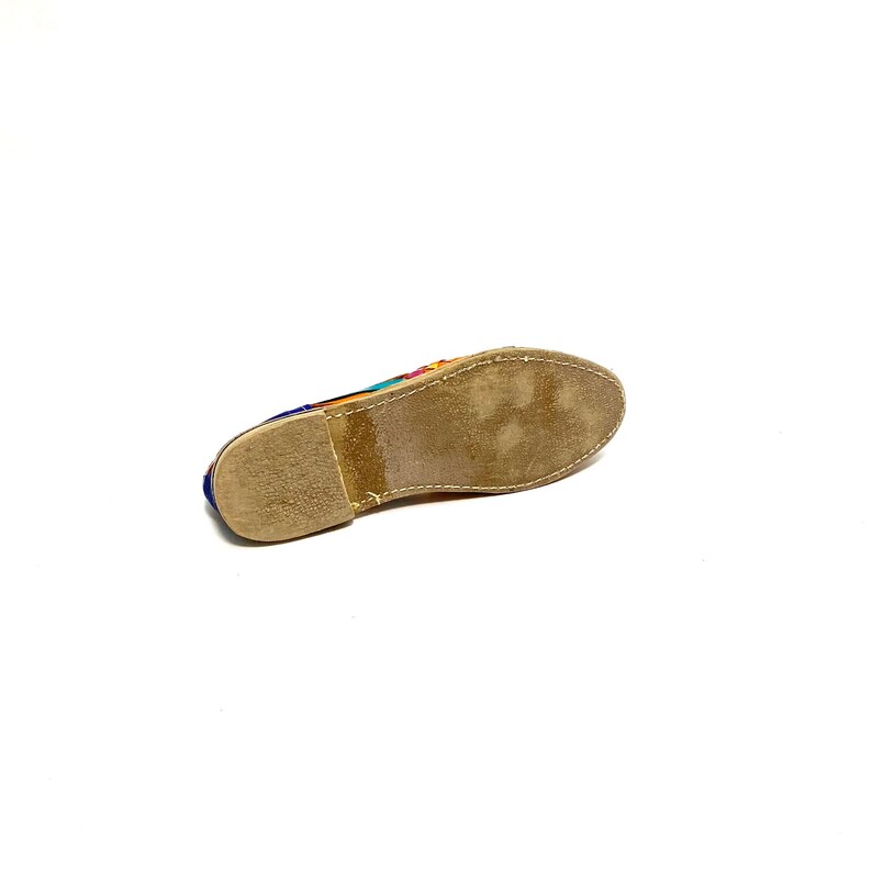 May include: A colourful, flat shoe with a stitched sole. The shoe's upper features a vibrant pattern of blue, orange, pink, and yellow. The sole is a light brown colour. The shoe is designed for casual wear.