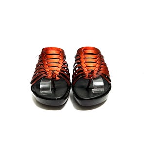 May include: A pair of orange leather sandals with a woven design and a black platform sole.