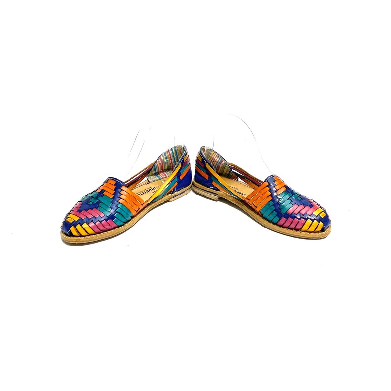 May include: A pair of colourful woven leather flats. The shoes feature a vibrant pattern of blue, orange, pink, and yellow. The soles are a natural tan colour, and the interior lining has a striped pattern.