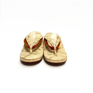 May include: A pair of white Japanese sandals with gold and orange accents. The sandals have a traditional design with a raised platform and a thong strap.