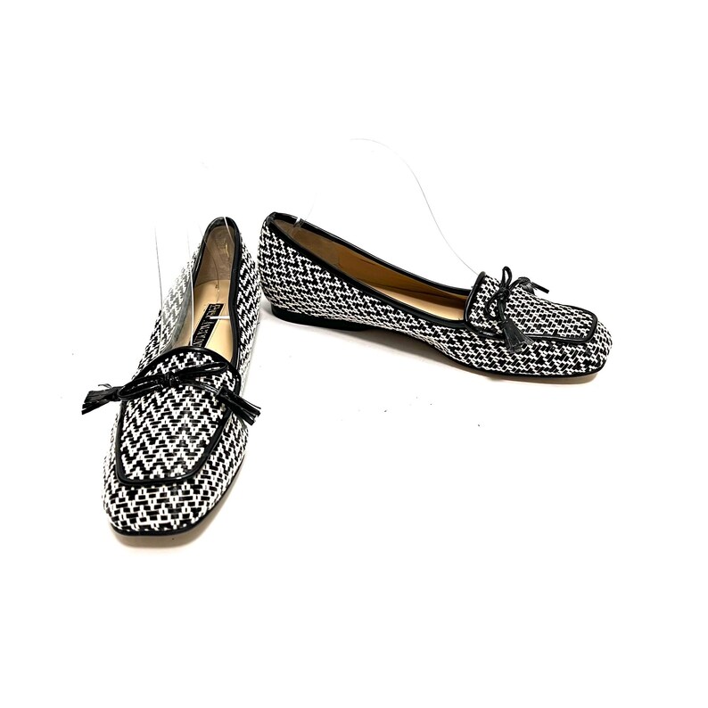 Op de afbeelding: Een paar zwart-witte geweven loafers met een vierkante neus en een kleine zwarte kwast. De schoenen hebben een zwarte bies en een lage hak. De schoenen staan op een witte achtergrond.