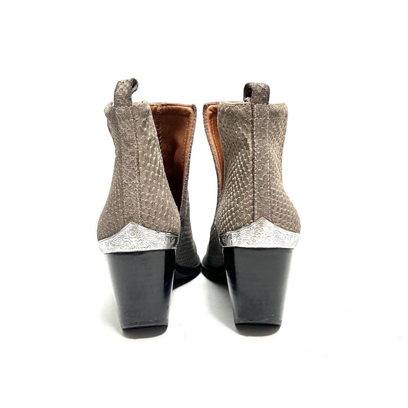 May include: A pair of ankle boots with a textured, snakeskin-like pattern in shades of grey and brown. The boots have black block heels and silver-coloured decorative accents at the heel. The interior is a light brown colour.