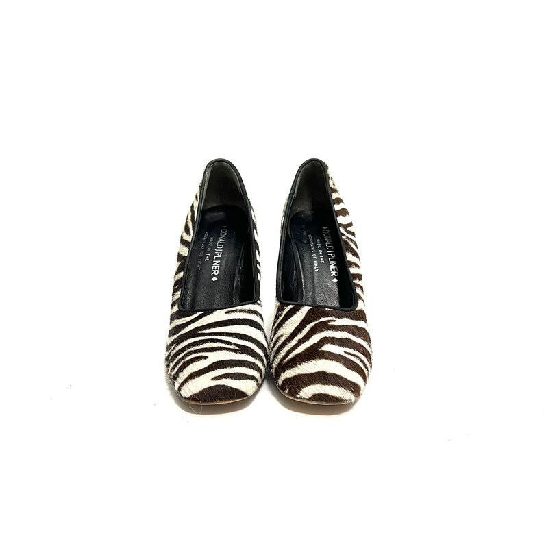 Pode incluir: Um par de sapatos de salto alto branco e preto com estampa de zebra e uma palmilha interior de couro preto. Os sapatos s&atilde;o da marca Donald Pliner e t&ecirc;m a inscri&ccedil;&atilde;o "Donald Pliner" na palmilha interior.