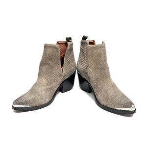 May include: A pair of grey ankle boots with a snakeskin pattern. The boots have a pointed toe with a silver metal cap, a black heel, and a V-shaped cut on the side. The boots are made of suede.