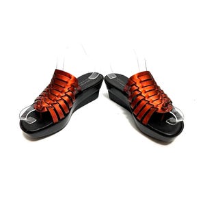 May include: A pair of orange leather woven sandals with a black platform wedge heel. The sandals have a toe loop and an ankle strap.