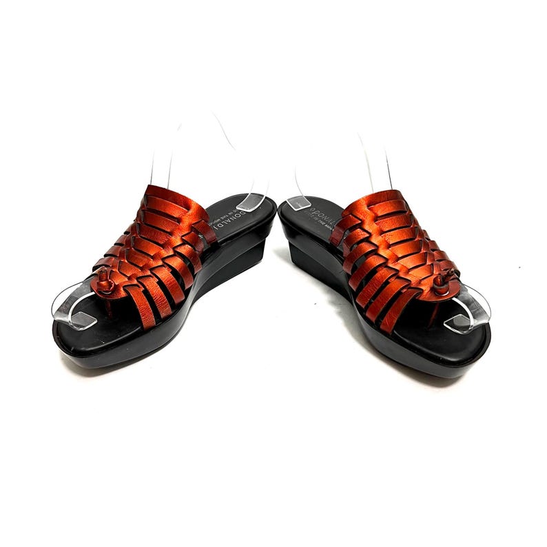 May include: A pair of orange leather woven sandals with a black platform wedge heel. The sandals have a toe loop and an ankle strap.