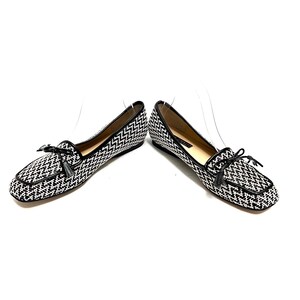 Op de afbeelding: Een paar zwart-wit patronen loafers met een vierkante neus. De schoenen hebben een zwarte leren rand en een kleine strik met een kwastje op de wreef. De schoenen staan tegen een witte achtergrond.