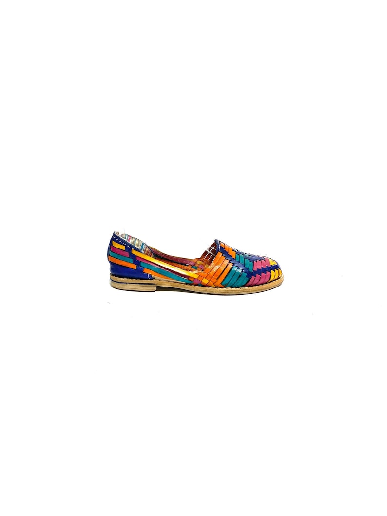 May include: A brightly coloured woven leather flat shoe. The shoe has a vibrant pattern of blue, orange, teal, and pink woven leather straps. The sole is light brown. The shoe is a slip-on style.