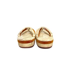 May include: A pair of traditional Japanese sandals, known as geta, with a white and gold patterned fabric upper and a brown wooden base.