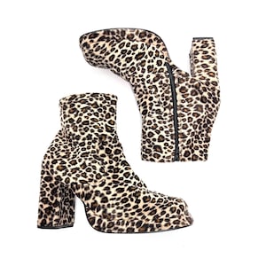 May include: A pair of ankle boots featuring a textured leopard print pattern in shades of brown, black, and cream. These boots have a square toe, a high block heel, a platform sole, and a black side zipper closure on the inner side of each boot.
