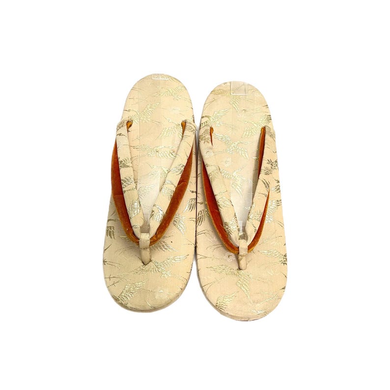 May include: A pair of beige Japanese sandals with orange velvet straps and a gold floral pattern.