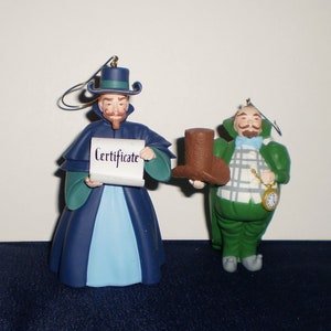 Peut inclure: Deux d&eacute;corations de No&euml;l repr&eacute;sentant des personnages du film 'L'&Eacute;trange No&euml;l de monsieur Jack'. La d&eacute;coration de gauche est une figurine bleue et verte tenant un parchemin sur lequel est inscrit 'Certificate'. La d&eacute;coration de droite est une figurine verte tenant un chapeau haut de forme brun.
