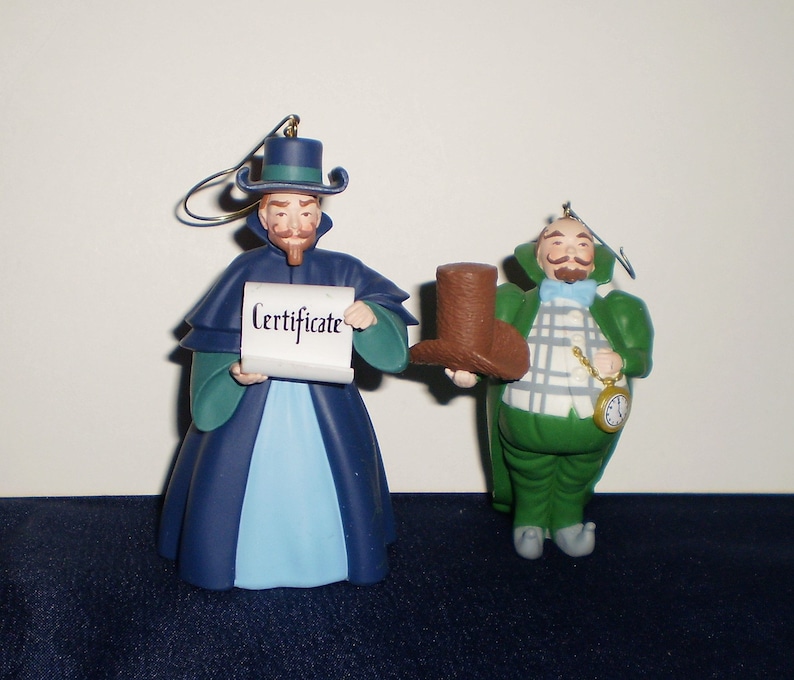 Peut inclure: Deux d&eacute;corations de No&euml;l repr&eacute;sentant des personnages du film 'L'&Eacute;trange No&euml;l de monsieur Jack'. La d&eacute;coration de gauche est une figurine bleue et verte tenant un parchemin sur lequel est inscrit 'Certificate'. La d&eacute;coration de droite est une figurine verte tenant un chapeau haut de forme brun.