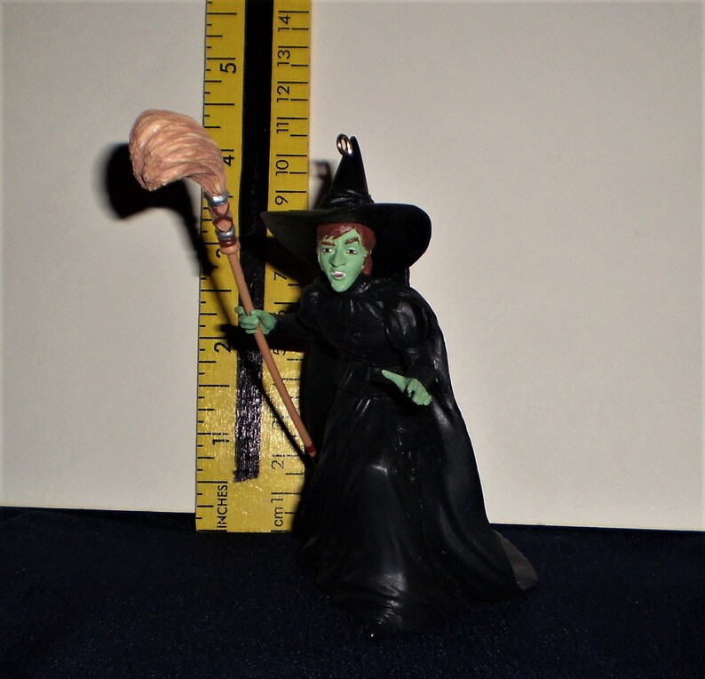 Peut inclure: Une figurine de sorci&egrave;re &agrave; la peau verte portant une robe et un chapeau noirs, tenant un balai brun. La figurine mesure environ 13 cm de haut.