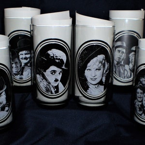 May include: Set of seven white glass tumblers with black and white images of famous silent film stars. The images include Charlie Chaplin, Buster Keaton, Harold Lloyd, and others.