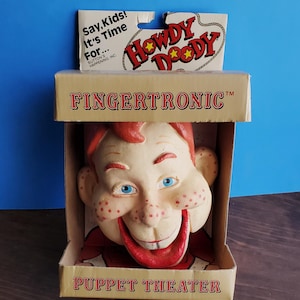 May include: A vintage Howdy Doody Fingertronic Puppet Theater toy. The puppet has a smiling face with red hair, freckles, and blue eyes. The box reads "Fingertronic" and "Puppet Theater". The packaging includes the text "Say, Kids! It's Time For..." and "Howdy Doody".