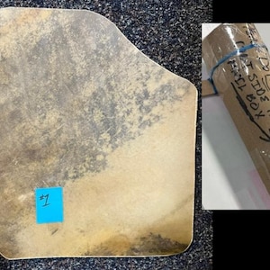 May include: A flat, irregularly shaped piece of tan and brown mottled material with a blue square sticker labeled #1. Next to it is a brown cardboard tube with a blue rubber band and handwritten text that reads DO NOT LEAVE OUTSIDE THE MAIL BOX.