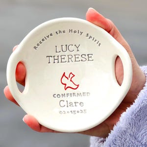 May include: White ceramic dish with two handles, featuring the text "Receive the Holy Spirit Lucy Therese Confirmed Clare 02-15-25" and a red dove graphic.