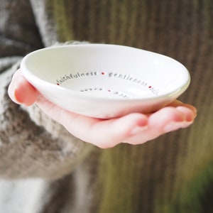 Peut inclure: Un petit plat &agrave; bijoux en c&eacute;ramique blanche avec les mots "fid&eacute;lit&eacute;, douceur, ma&icirc;trise de soi, bont&eacute;, patience, amour, joie, paix, longanimit&eacute;" &eacute;crits autour du bord en lettres grises avec des points rouges entre chaque mot.
