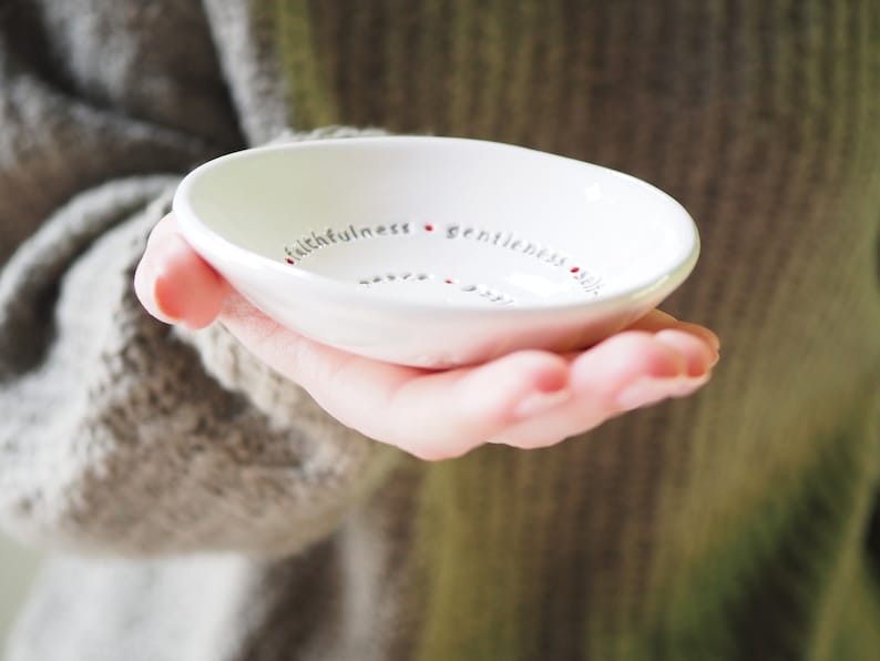 Peut inclure: Un petit plat &agrave; bijoux en c&eacute;ramique blanche avec les mots "fid&eacute;lit&eacute;, douceur, ma&icirc;trise de soi, bont&eacute;, patience, amour, joie, paix, longanimit&eacute;" &eacute;crits autour du bord en lettres grises avec des points rouges entre chaque mot.