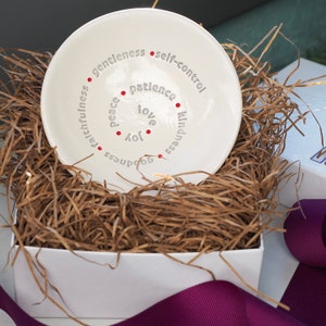 Peut inclure: Plat en c&eacute;ramique blanche avec un cercle de mots en lettres grises autour du bord. Les mots sont "gentleness", "self-control", "patience", "love", "joy", "kindness", "goodness", "faithfulness", "peace". Il y a des points rouges entre chaque mot.