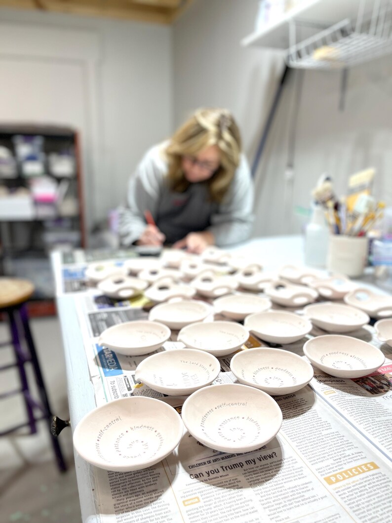 A blonde haired women stands at a table with several handmade bowls on it.